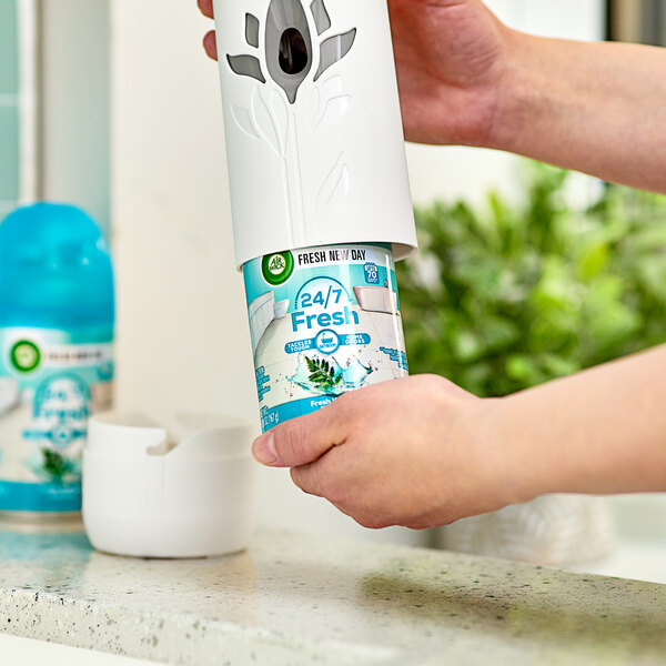 A hand holding a white container of Air Wick Fresh Waters scented air freshener.