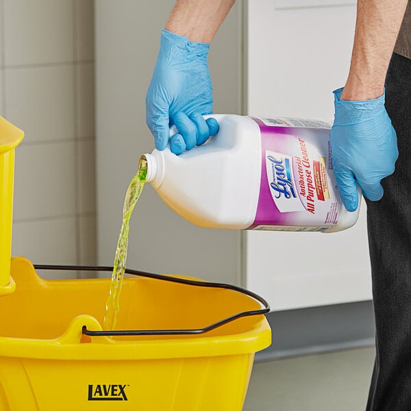 A hand in a glove pouring Professional Lysol Antibacterial Concentrated All-Purpose Cleaner into a bucket.