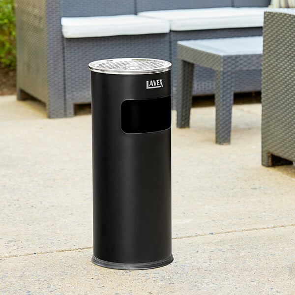 A black round steel cigarette receptacle with a round lid on a concrete patio.