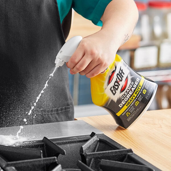 A hand pouring Easy-Off Heavy-Duty Cleaner Degreaser onto a stove top.