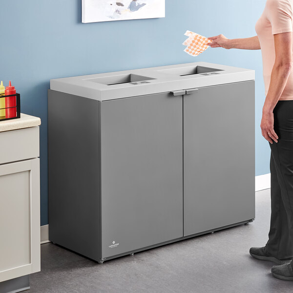 A large dark gray steel rectangular trash can with two separate openings for waste disposal.