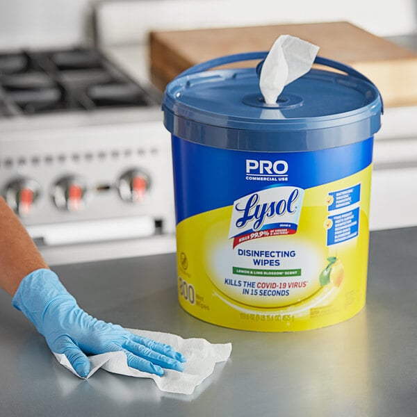 A hand in a blue glove uses Lysol Disinfecting Wipes to clean a counter.