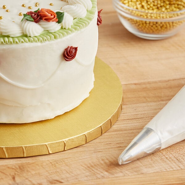 A Baker's Lane gold cake drum on a counter with a frosted cake.