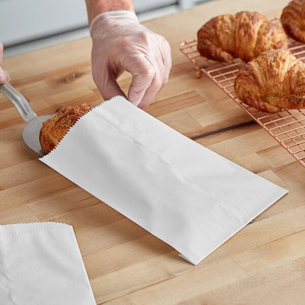 A person using a pizza cutter to cut a croissant and put it in a customizable white gourmet bag.