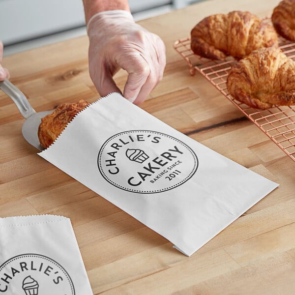 A person putting a croissant into a customizable white gourmet bag.