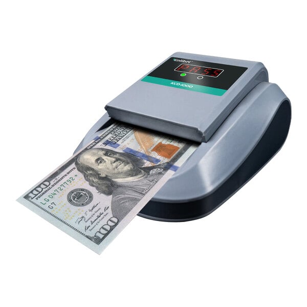 A Kolibri KCD-1000 counterfeit detector on a counter with a digital display showing a hundred dollar bill.