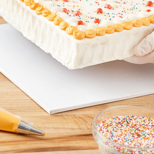 A person using a Baker's Lane white cake drum to cut a cake.