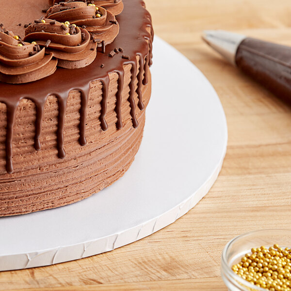 A chocolate cake on a Baker's Lane white cake drum on a table
