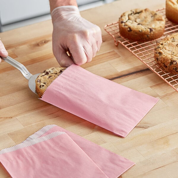 A hand putting a pink cookie in a customizable pink paper bag.