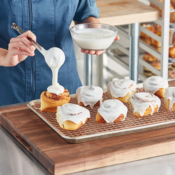 A person pouring icing onto a cinnamon roll.