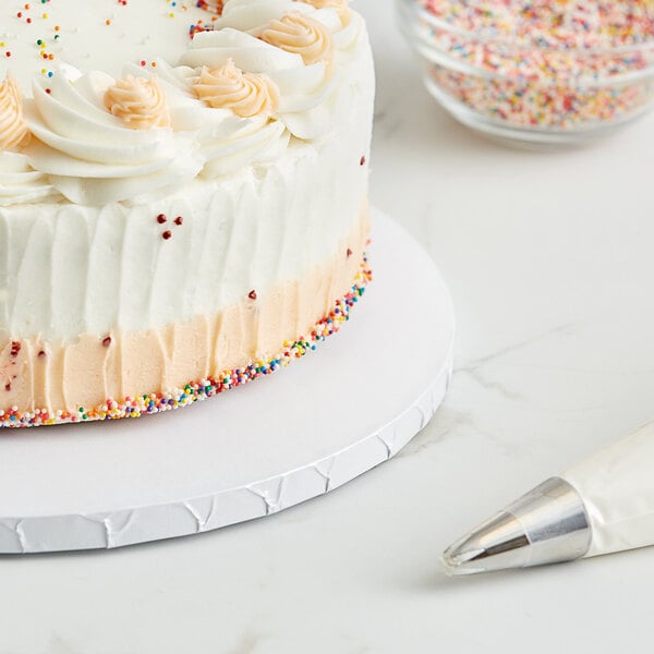 A white cake with sprinkles on a Baker's Lane cake drum on a table.