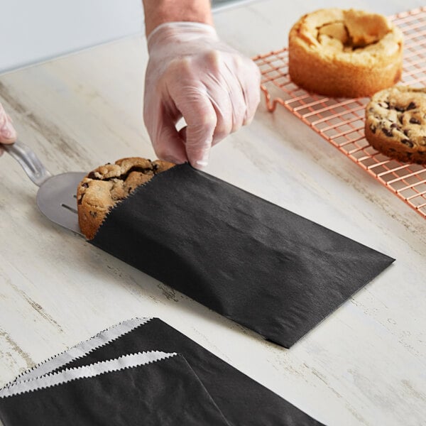 A hand putting a chocolate chip cookie in a customizable black paper bag.