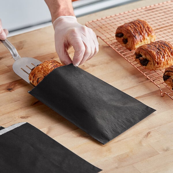 A hand putting a pastry in a black customizable gourmet bag.