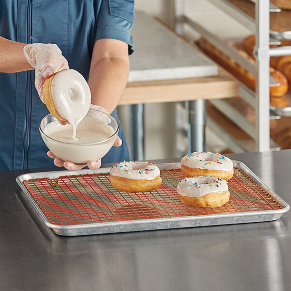 A woman pouring white frosting into a bowl of doughnuts.