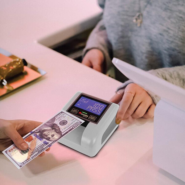 A person using a Cassida Quattro 4-way counterfeit detector to check paper money at a bar counter.
