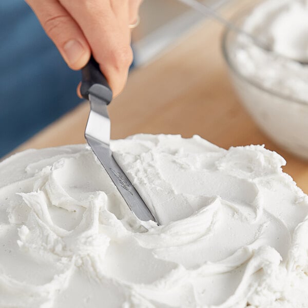 A hand holding a knife cutting into white Brill Vanilla Light 'n Fluffy Buttercreme Frosting.