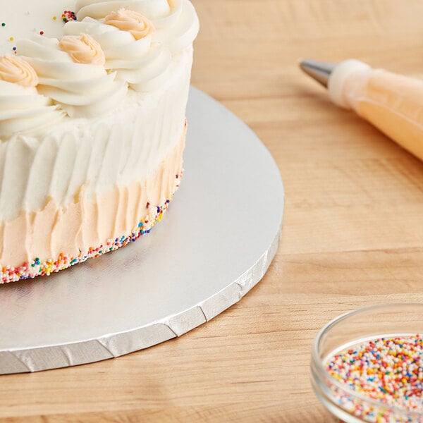 A Baker's Lane cake with sprinkles on a silver cake drum on a table.