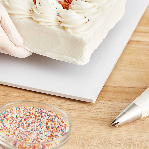 A hand using a knife to cut a white cake on a Baker's Lane white cake drum.