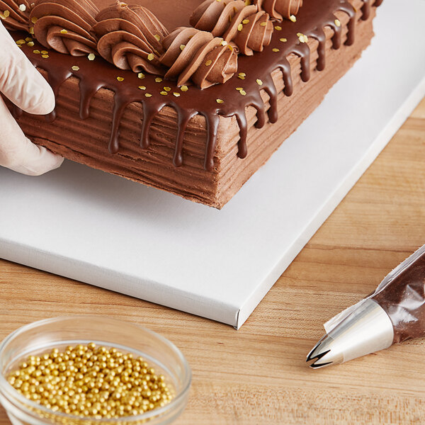 A person using a gloved hand to cut a white cake on a Baker's Lane cake drum.