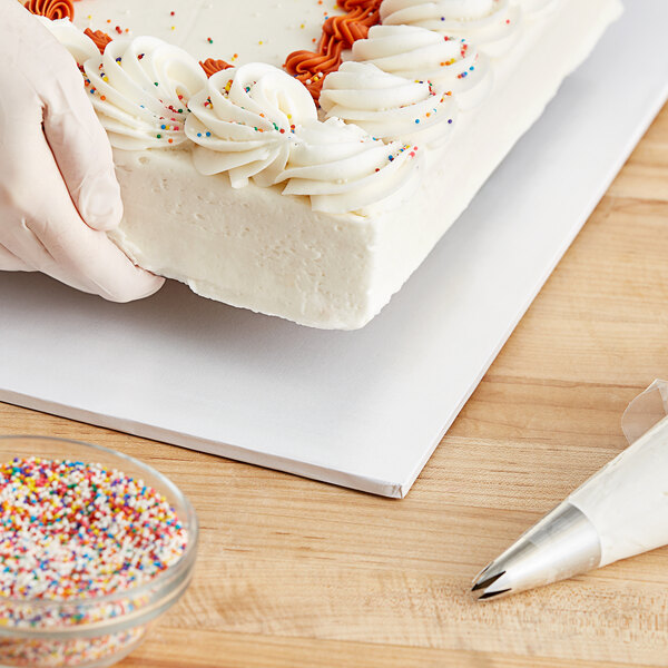 A person holding a cake on a white Baker's Lane cake drum.