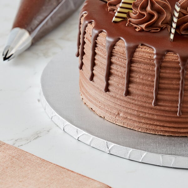 A chocolate cake on a Baker's Lane silver cake drum on a table in a bakery display.