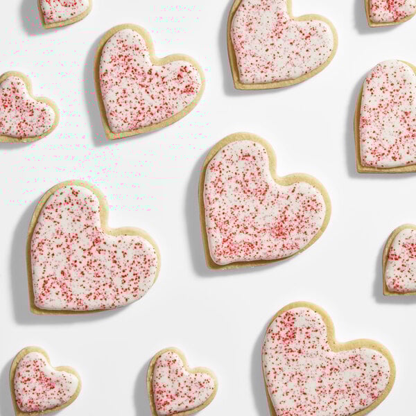 A collection of heart-shaped cookies decorated with white icing and red sanding sugar.