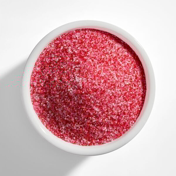 A white bowl filled with fine red and pink sanding sugar.