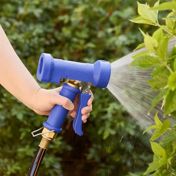 A hand holding a blue Regency front trigger spray nozzle spraying water on plants.