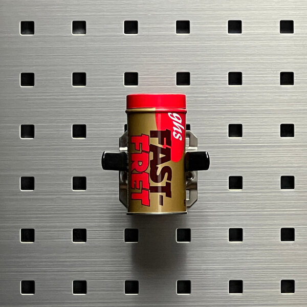 A Triton Products stainless steel spring clip holding a small container on a metal surface.