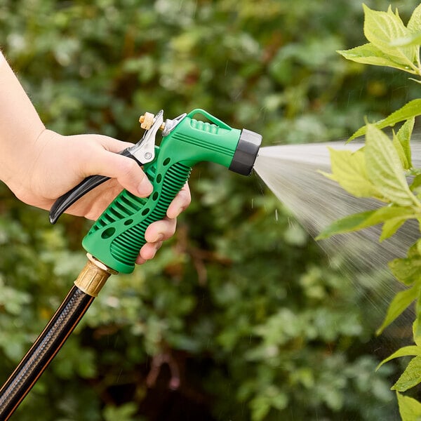 A hand holding a green and black hose spraying water with a Regency green metal garden spray nozzle.