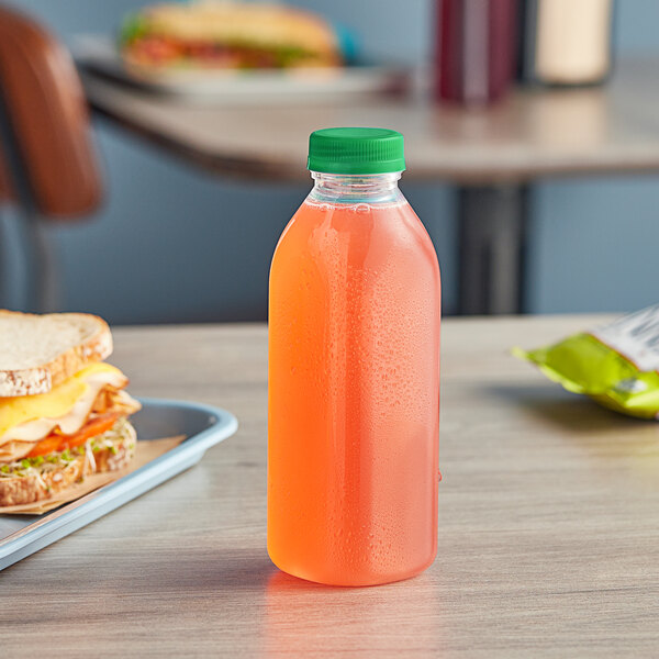 A 16 oz Square Milkman juice bottle filled with orange liquid next to a sandwich on a counter.