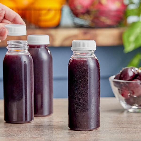 A hand pouring juice into a white 8 oz. round PET juice bottle.