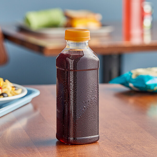 A 14.5 oz. Square PET clear juice bottle with an orange cap on a table.