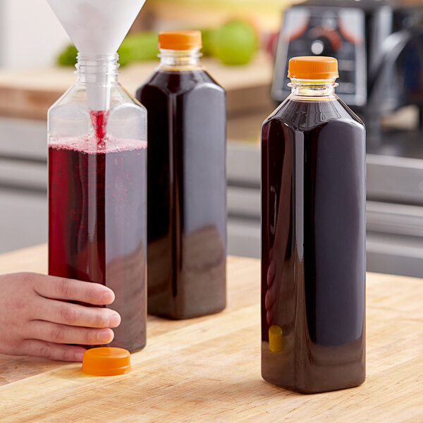 A hand pours juice into a clear PET juice bottle with an orange lid.