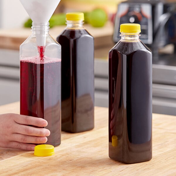 A hand using a funnel to pour liquid into a clear square juice bottle.