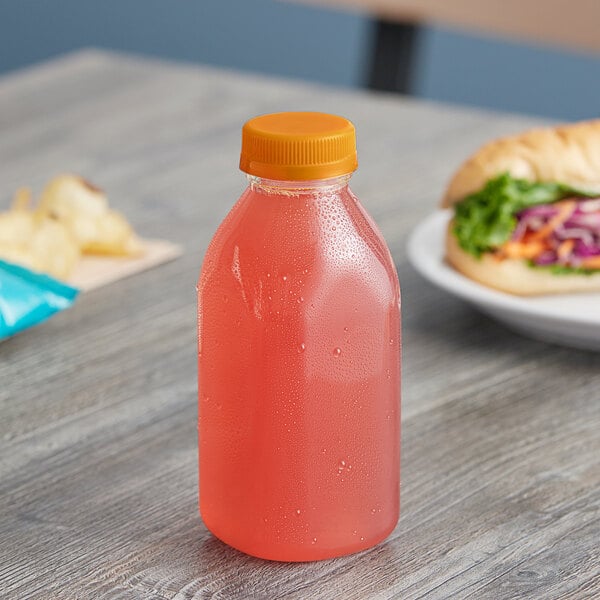 A Square Milkman juice bottle filled with pink liquid sits on a table next to a sandwich.