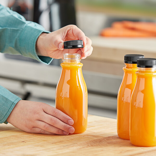 A person pouring orange juice into a round clear carafe.