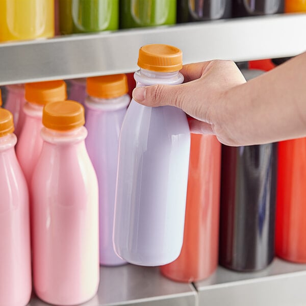 A hand holding a round clear juice bottle with an orange lid.