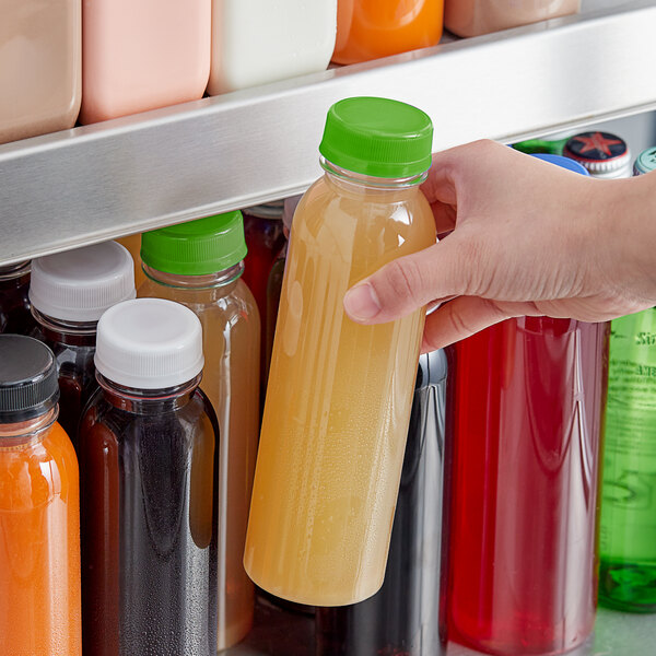 A hand holding a 12 oz. round clear PET juice bottle with a lime green lid.