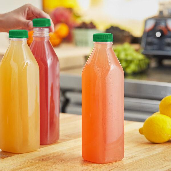 A hand holding a 32 oz. clear plastic juice bottle with yellow liquid next to a lemon.