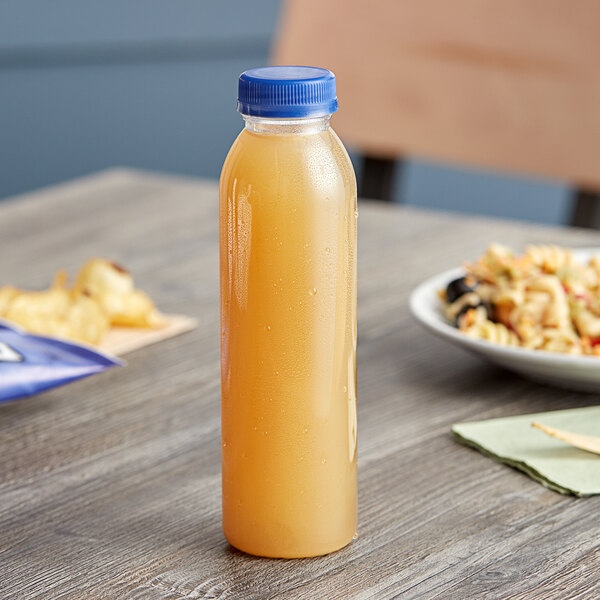A 12 oz. round clear rPET juice bottle with a blue cap on a table next to a plate of food.