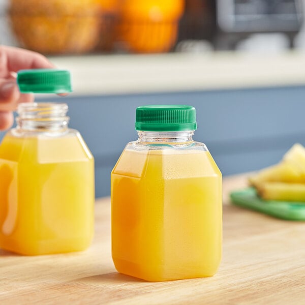 A hand holding a Square PET clear juice bottle with orange liquid and a green lid.