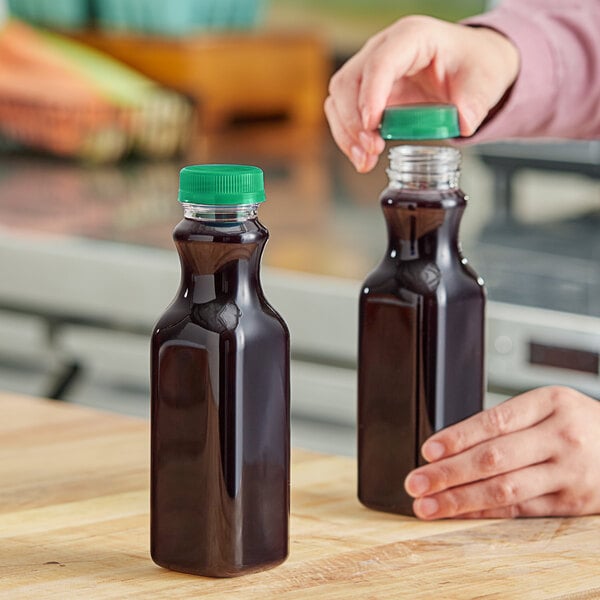 A person pouring juice into a 12 oz. square PET clear carafe juice bottle with a green lid.