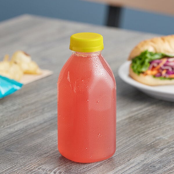 A Square Milkman juice bottle with yellow lid filled with pink liquid on a counter next to a sandwich.
