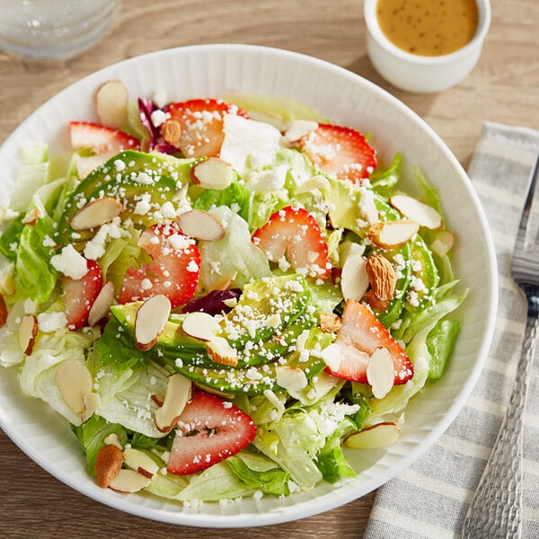 A bowl of California salad with strawberries and almonds on a white plate.