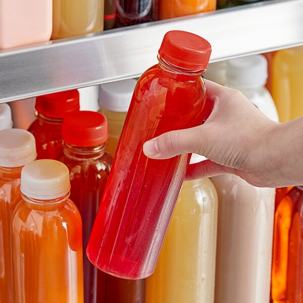 A hand holding a 16 oz. clear plastic juice bottle with red liquid inside.
