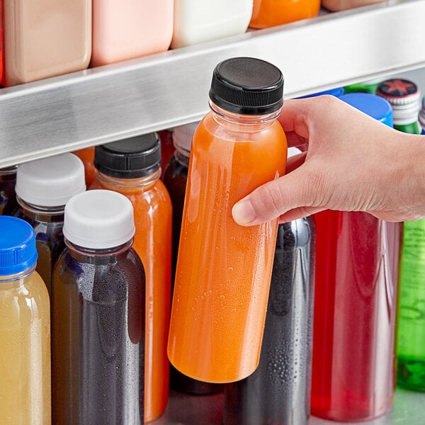 A hand holding a 12 oz. clear round PET juice bottle with orange juice inside.