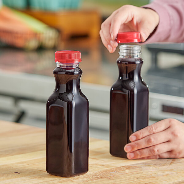 A person pouring juice into a Square PET clear carafe with a red cap.