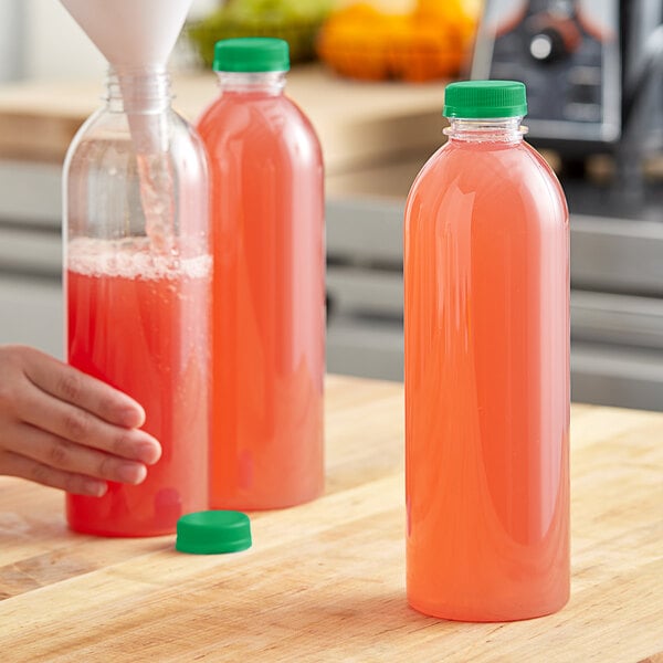 A hand pouring pink juice into a 32 oz. clear juice bottle with a green lid.