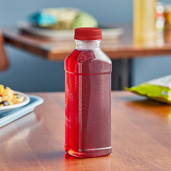 A 15.2 oz. Square clear PET juice bottle with a red liquid in it on a table.